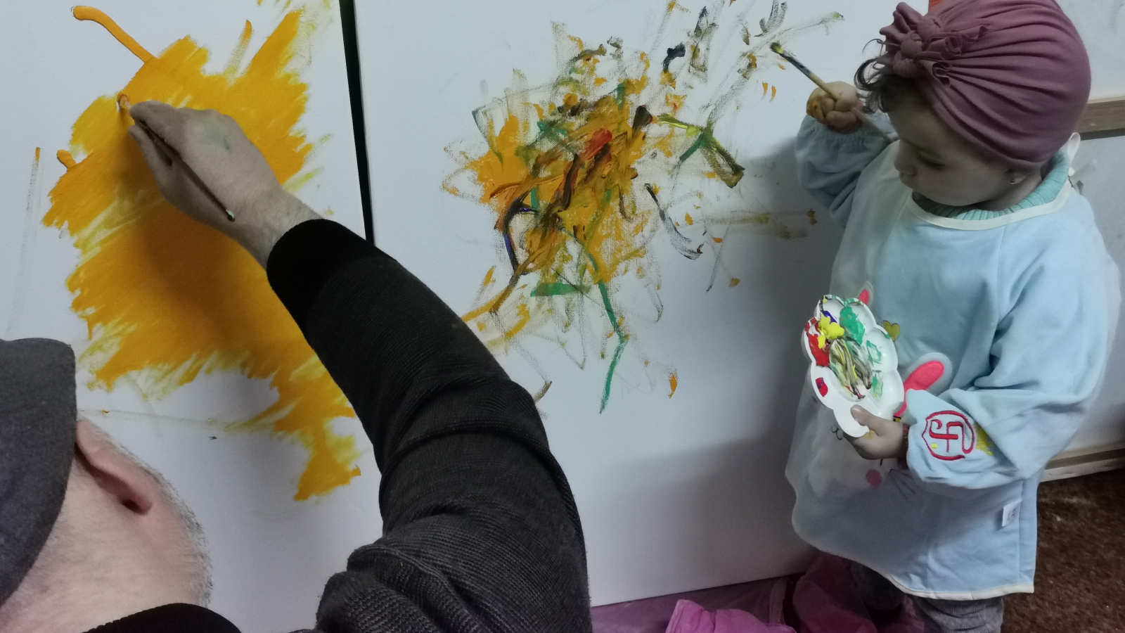 Adult and child painting abstract art on canvases together.